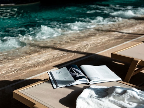 Un livre intitulé « Histoire de l’évolution d’une maladie » est posé sur une chaise longue au bord d’une piscine, où l’on aperçoit des vagues.