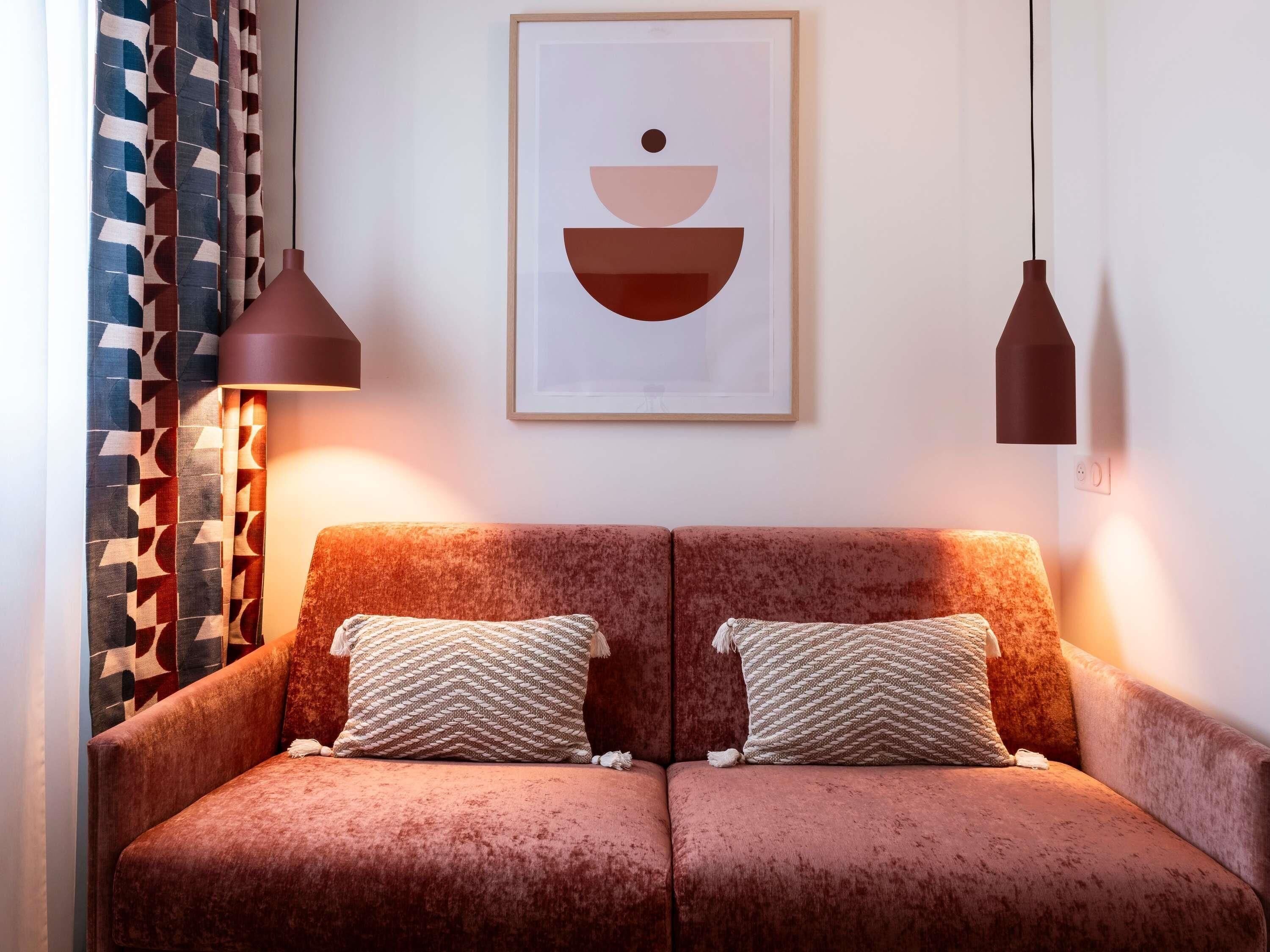 A cozy room with a two-seater sofa, patterned cushions, and a framed abstract artwork above.