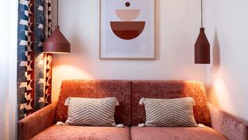 A cozy room with a two-seater sofa, patterned cushions, and a framed abstract artwork above.