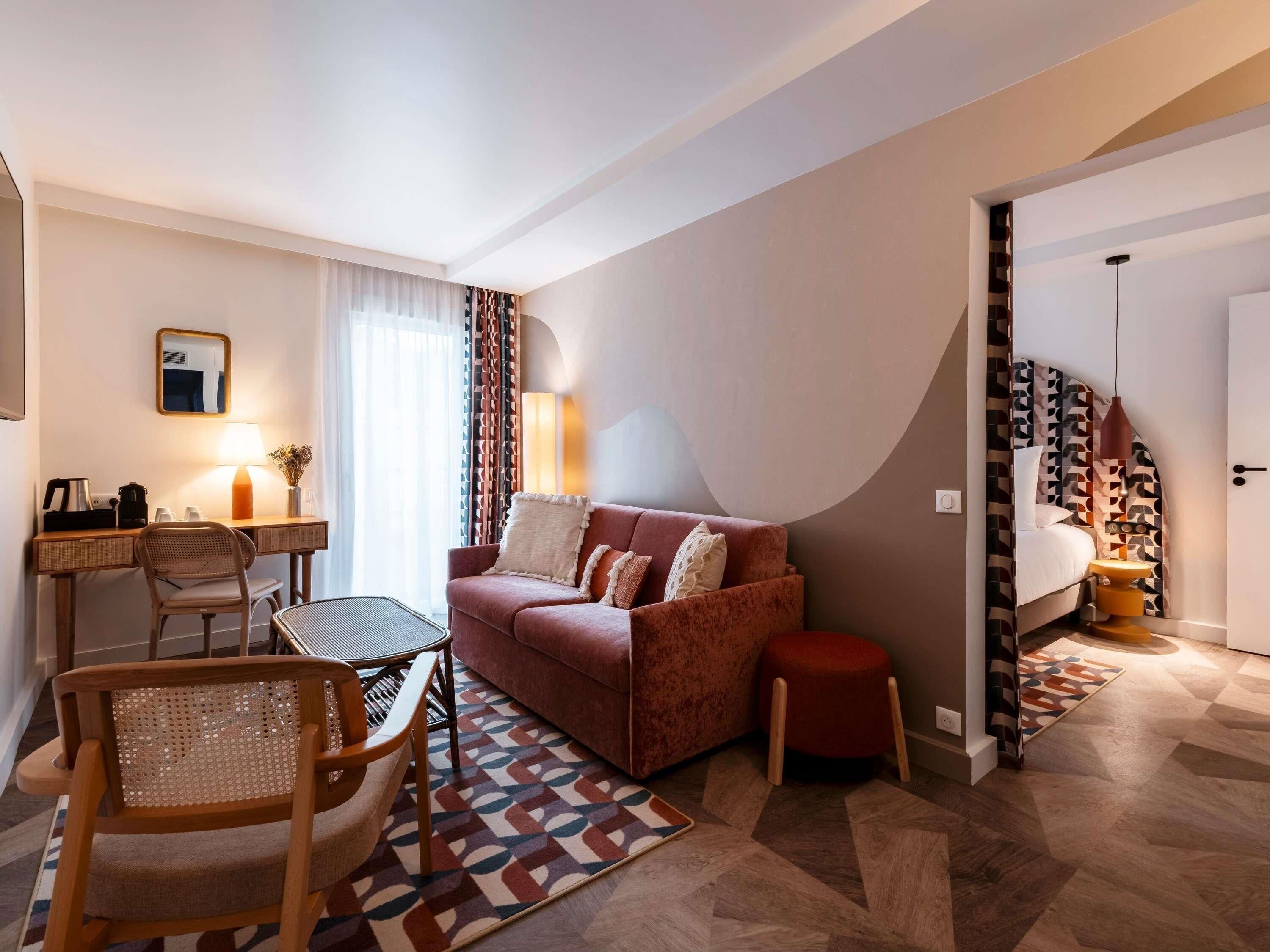 Habitaci ón de hotel con sofá, escritorio con lámpara, una silla y alfombra estampada.