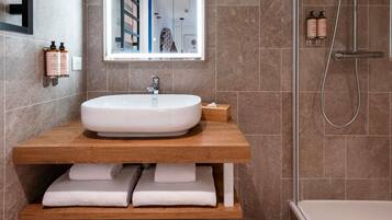 Une salle de bain moderne avec un grand lavabo ovale, un meuble-lavabo en bois et une douche à l’italienne.