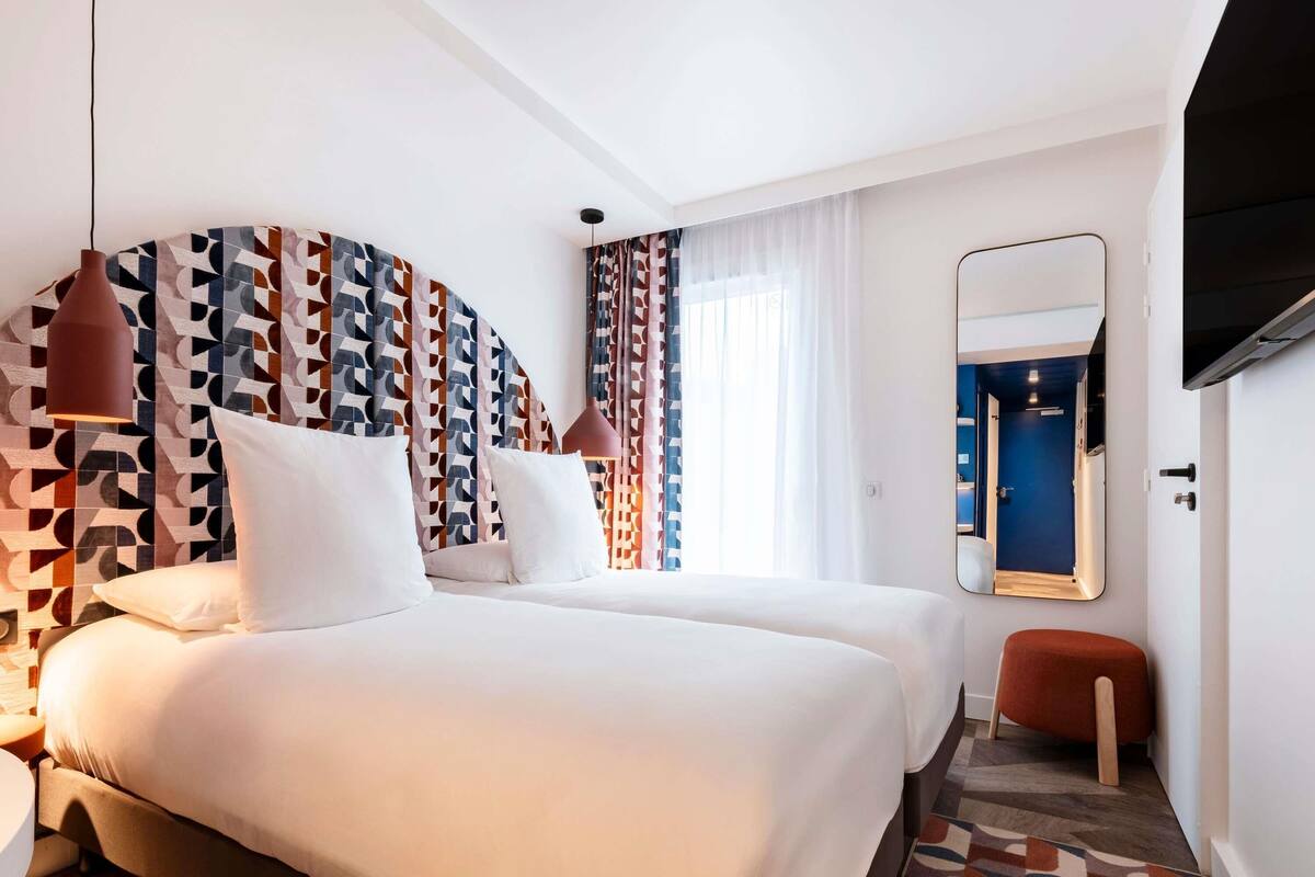 A hotel room with two beds, a large mirror, a TV, and a patterned wall.