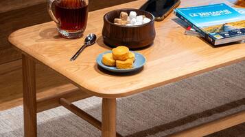 A wooden table with a glass of tea, a bowl of marshmallows, a spoon, a smartphone, and a book.