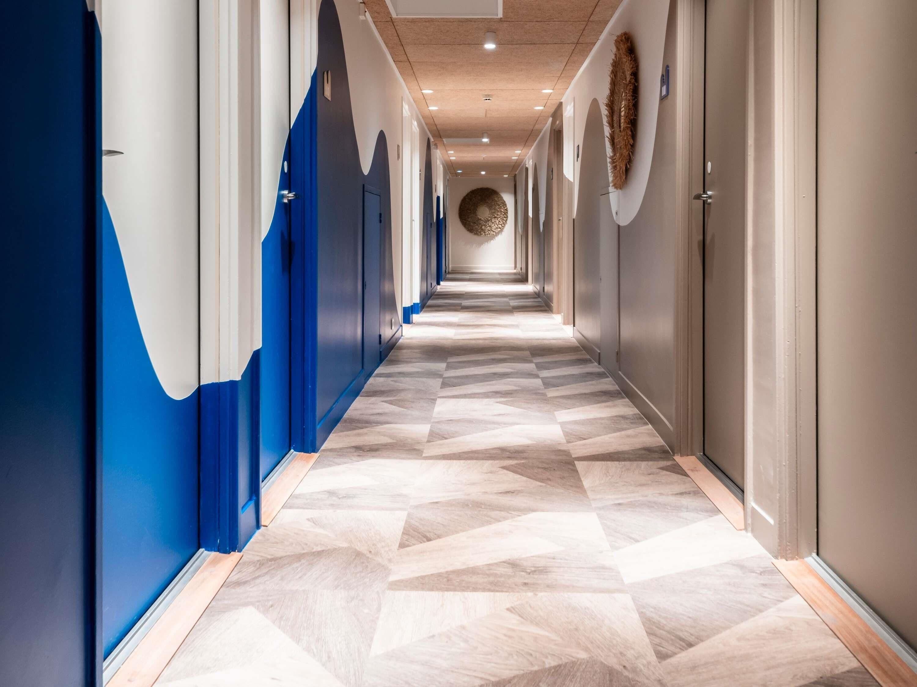 A hotel corridor with a geometric patterned floor, blue and white walls, and a circular wall decoration.