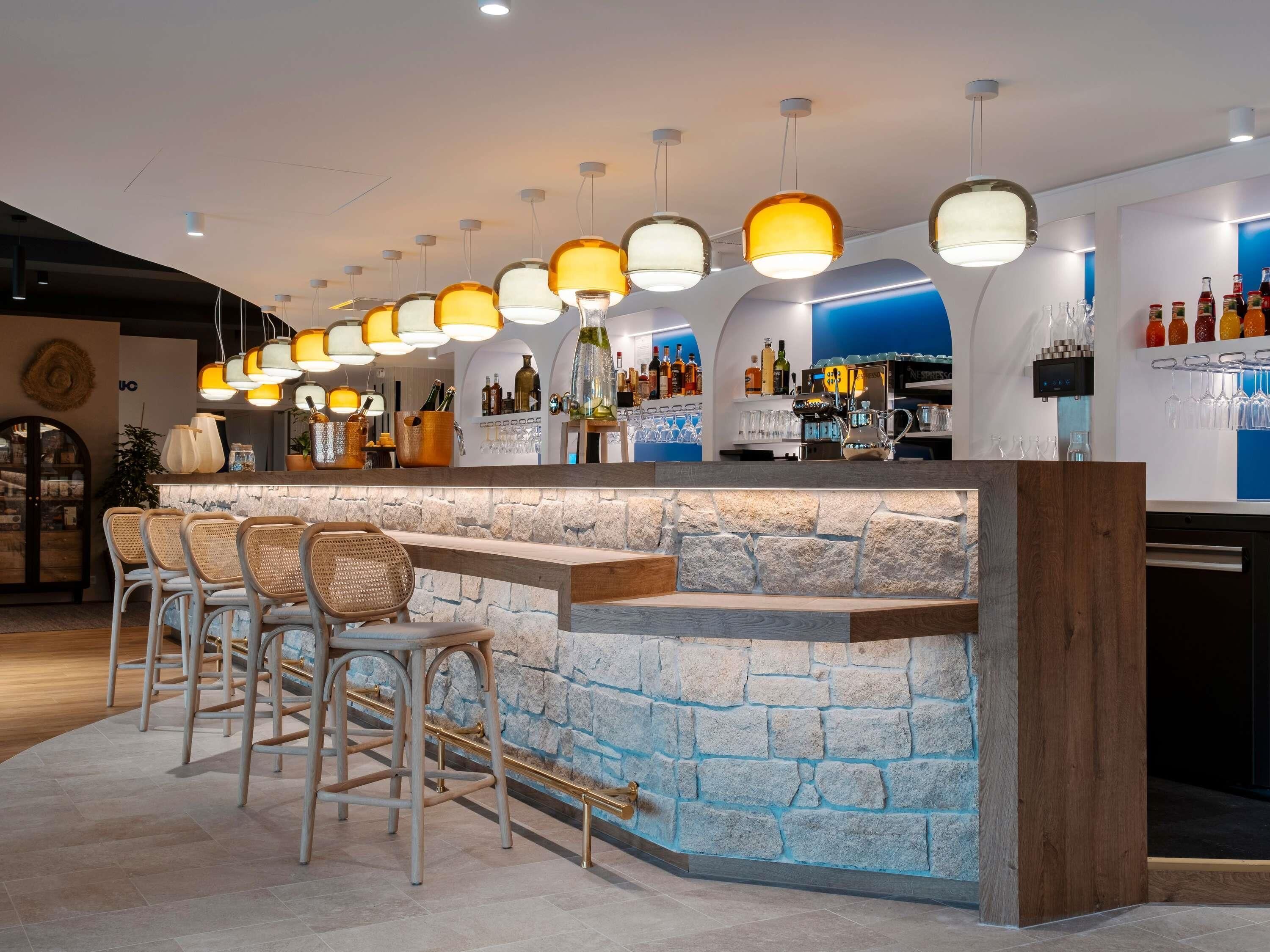 A bar area with a stone counter, multiple hanging pendant lights, and a selection of bottles and glasses on shelves.