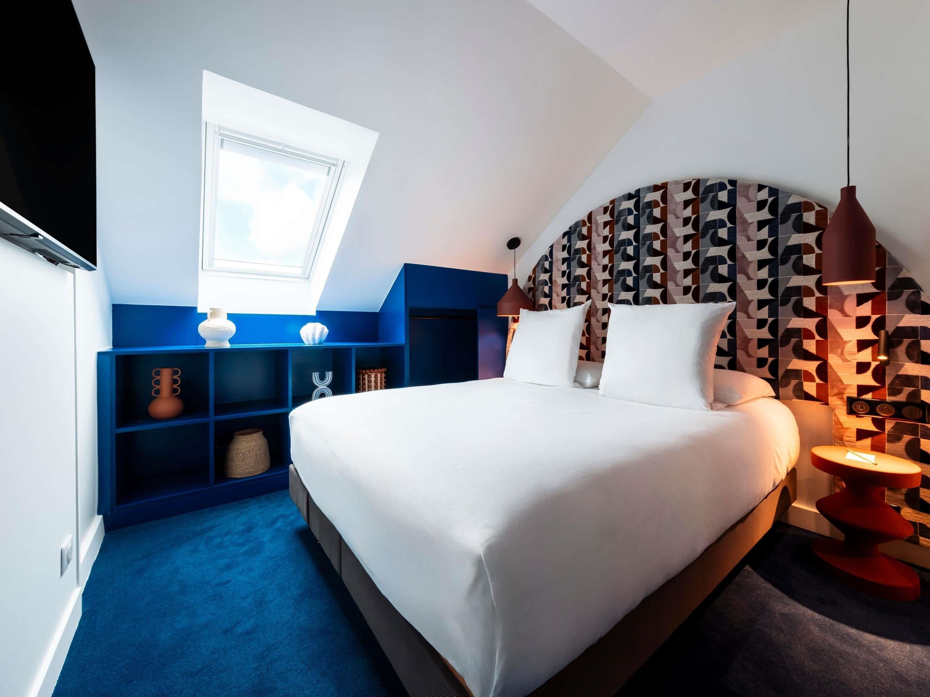 Un dormitorio moderno con una cama grande, un tragaluz, un estante azul y un cabecero estampado.