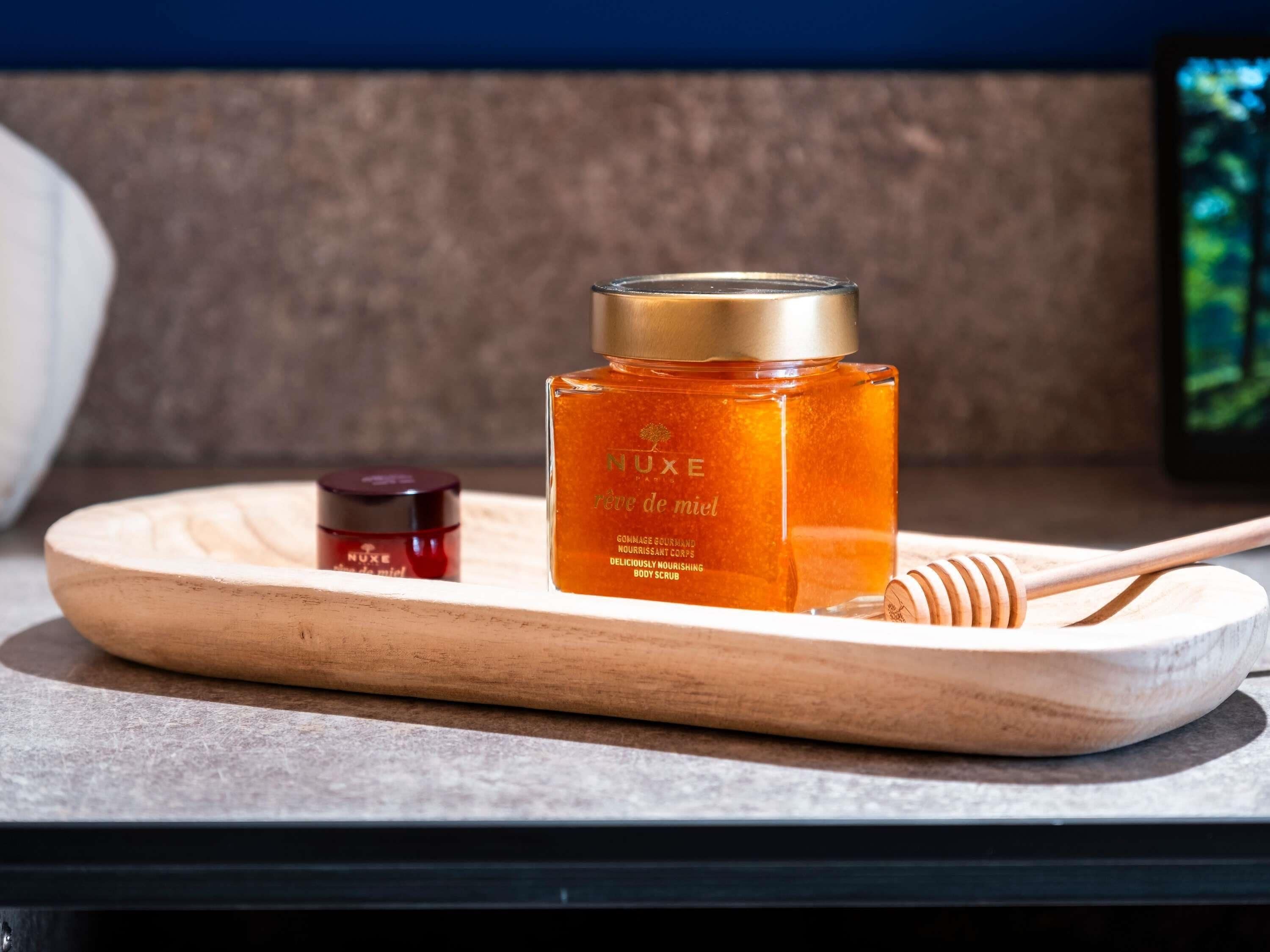 A wooden tray with a honey jar and a honey dipper on a table.