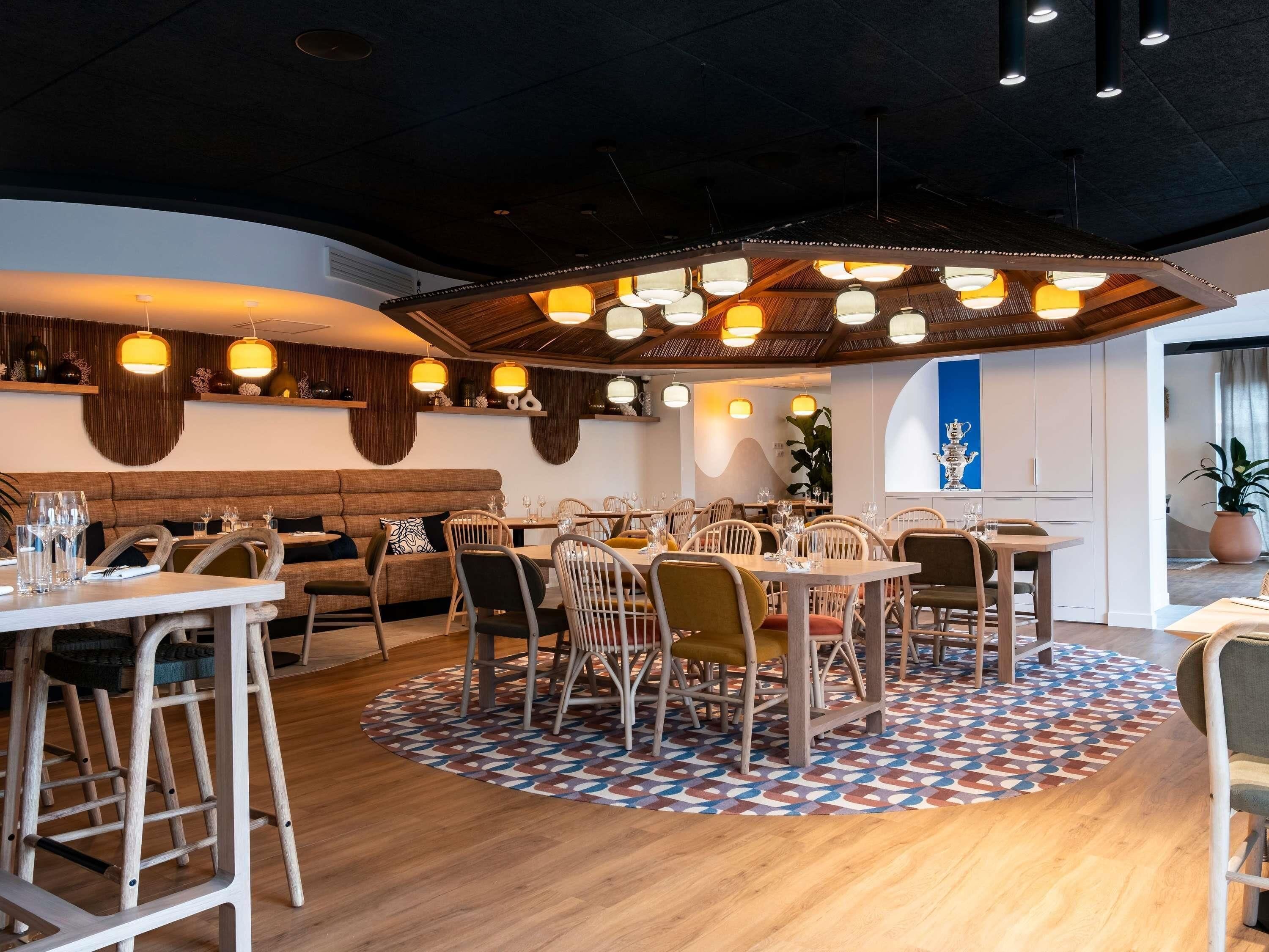 A restaurant interior with round tables, wooden chairs, and hanging pendant lights.
