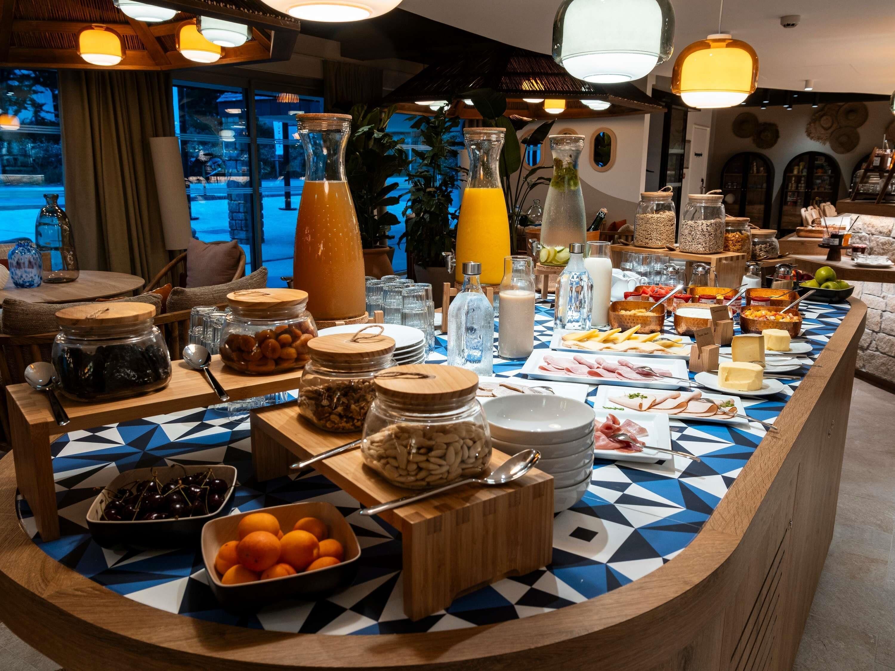 A buffet setup with various food items and beverages, including fruits, cheeses, and a large orange juice dispenser.