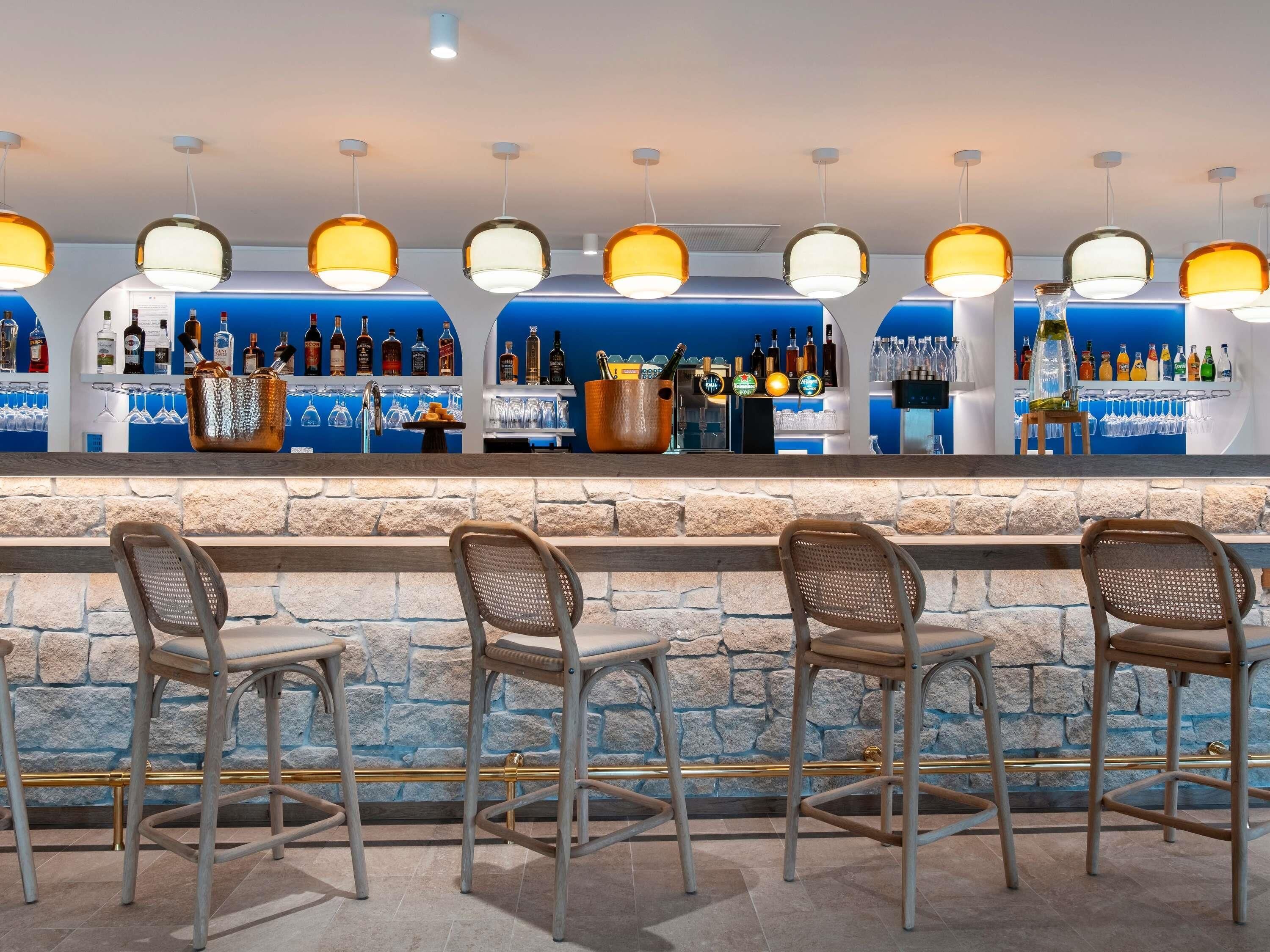 A bar area with a stone wall, multiple bar stools, and a variety of bottles and glasses on shelves.