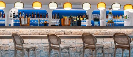 A bar area with a stone wall, multiple bar stools, and a variety of bottles and glasses on shelves.