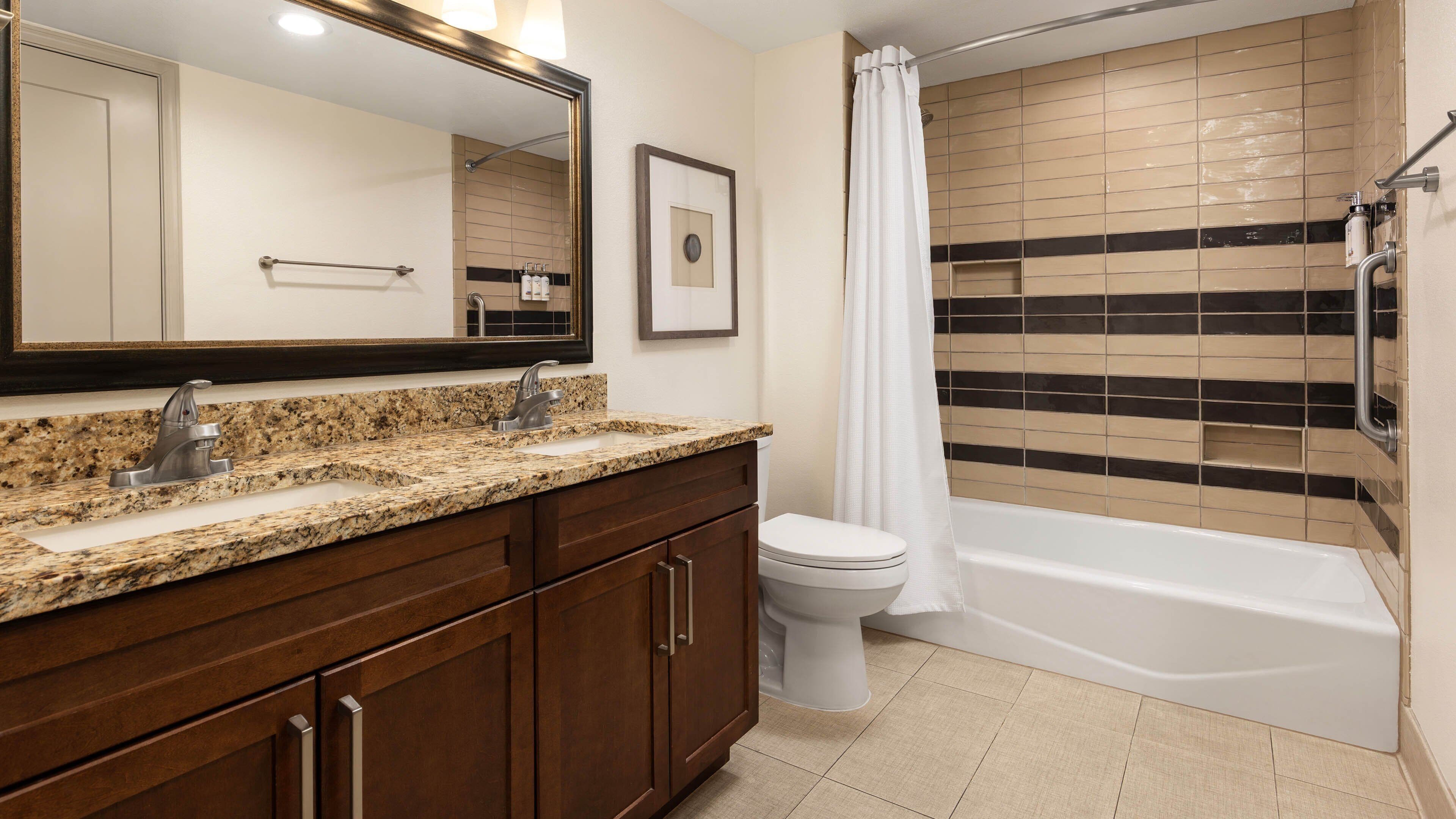 A bathroom with a double sink vanity, a toilet, and a bathtub.