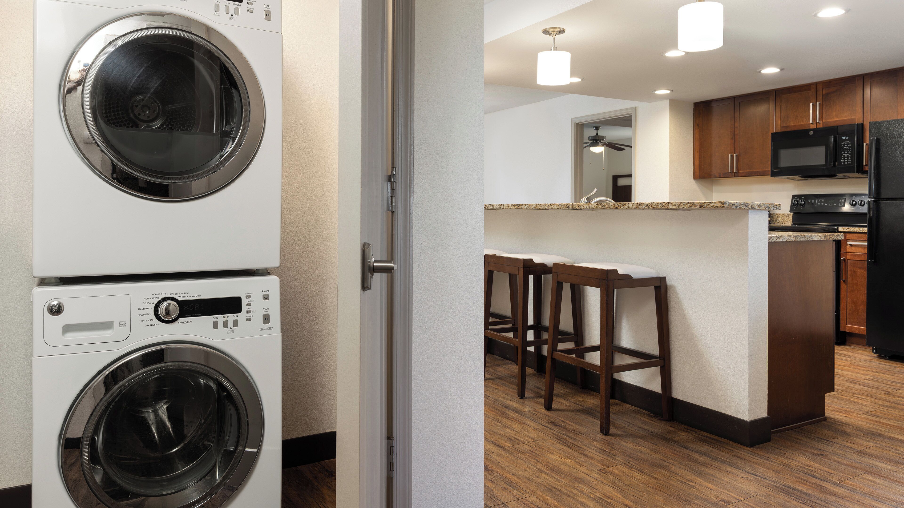 A laundry room with two washing machines and a kitchen area with wooden cabinets, a microwave, and a refrigerator.