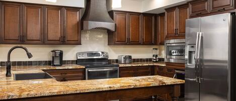 Una cocina moderna con armarios de madera oscura, encimeras de granito, electrodomésticos de acero inoxidable y una isla central con asientos.