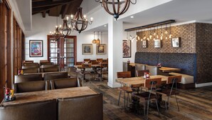 A restaurant interior with wooden tables and chairs, hanging lights, and a brick wall.