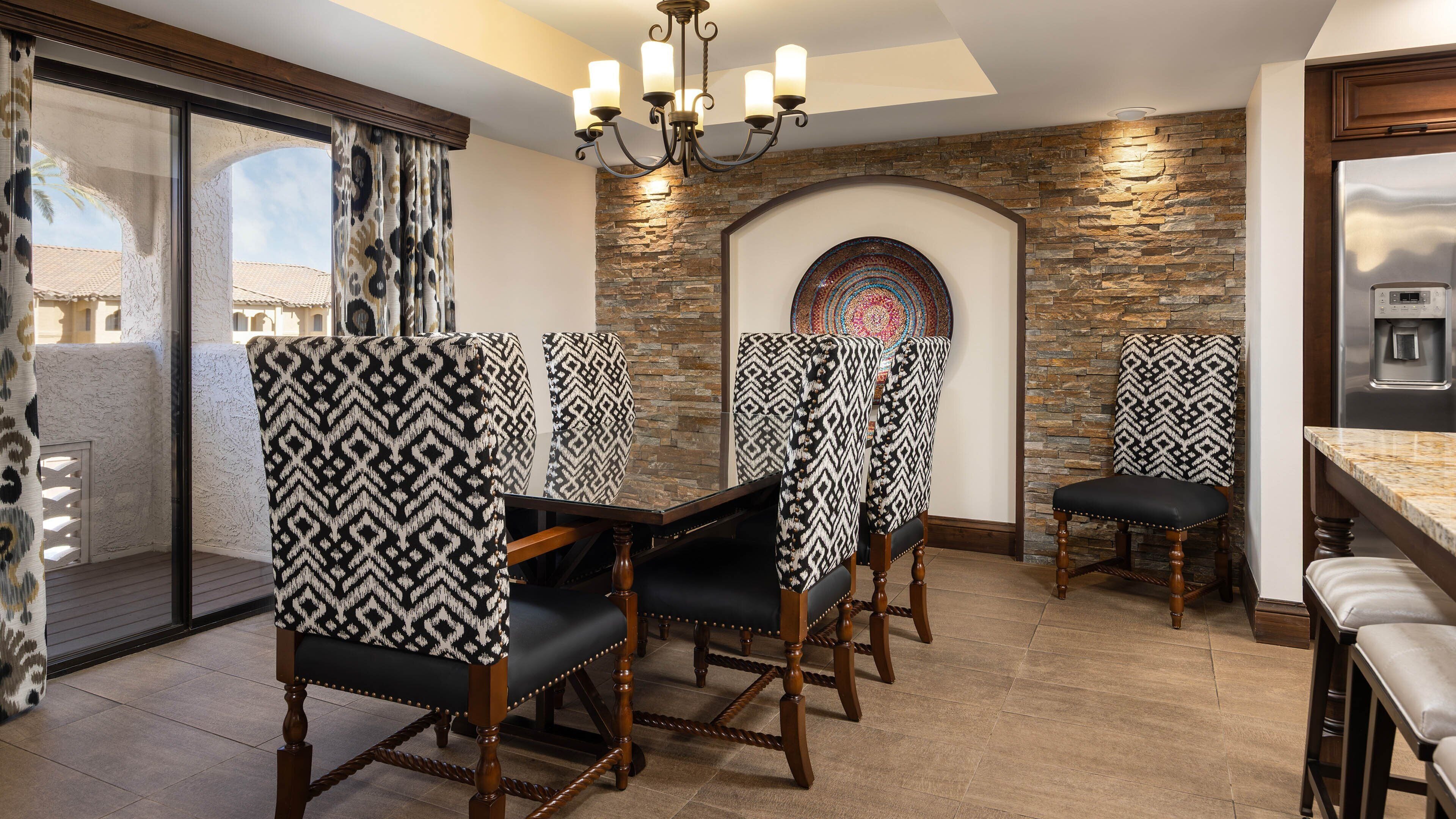 A dining area with patterned chairs, a stone wall, and a modern chandelier.