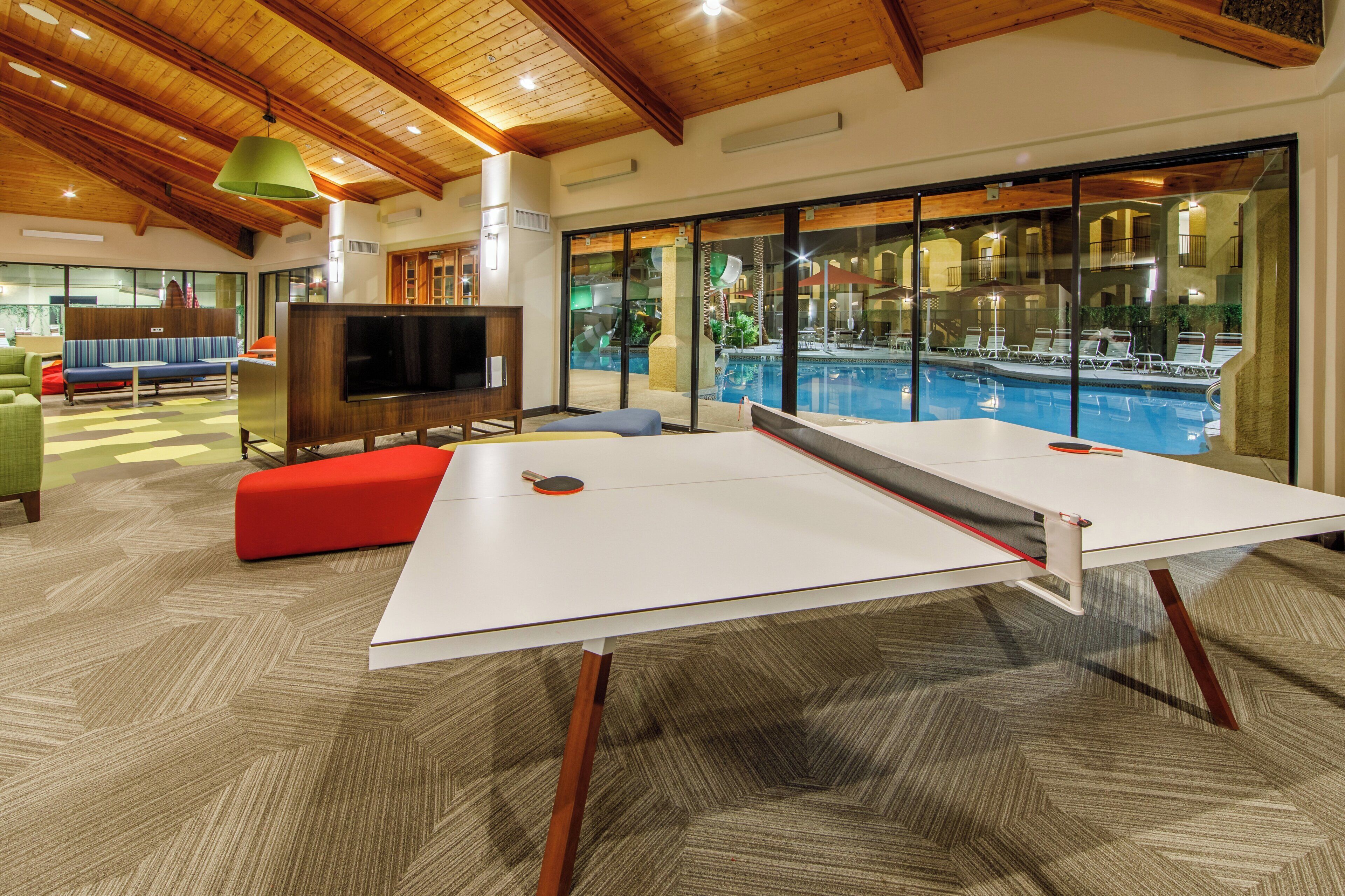 A room with a ping pong table, a television, and a pool view.