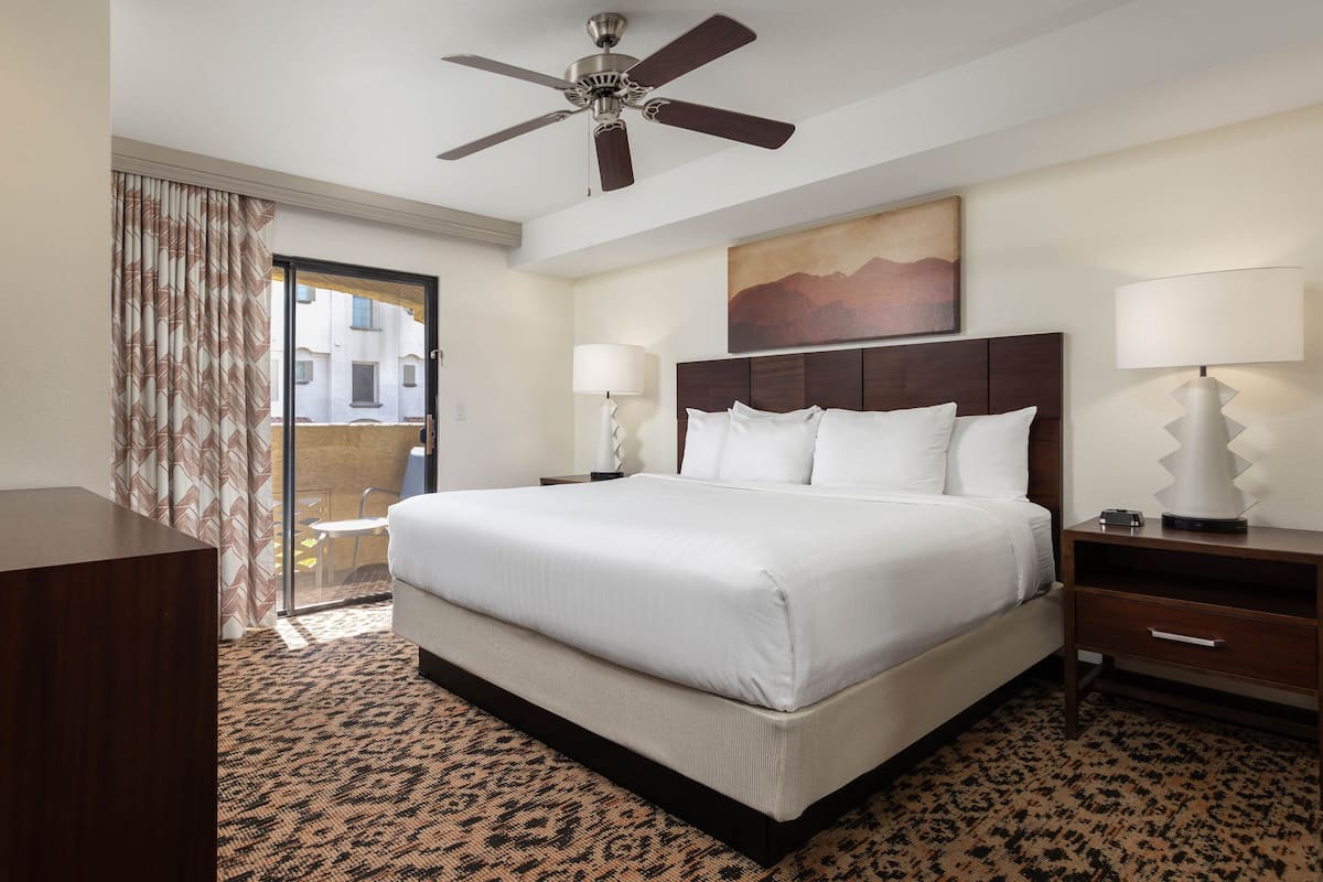 A hotel room with a large bed, a ceiling fan, a TV, a desk, and a window with curtains.