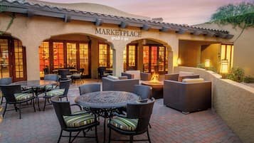 Un patio al aire libre con mobiliario de mimbre y un pozo de fuego, debajo de un edificio con un letrero que dice 'MARKETPLACE grab & go'.