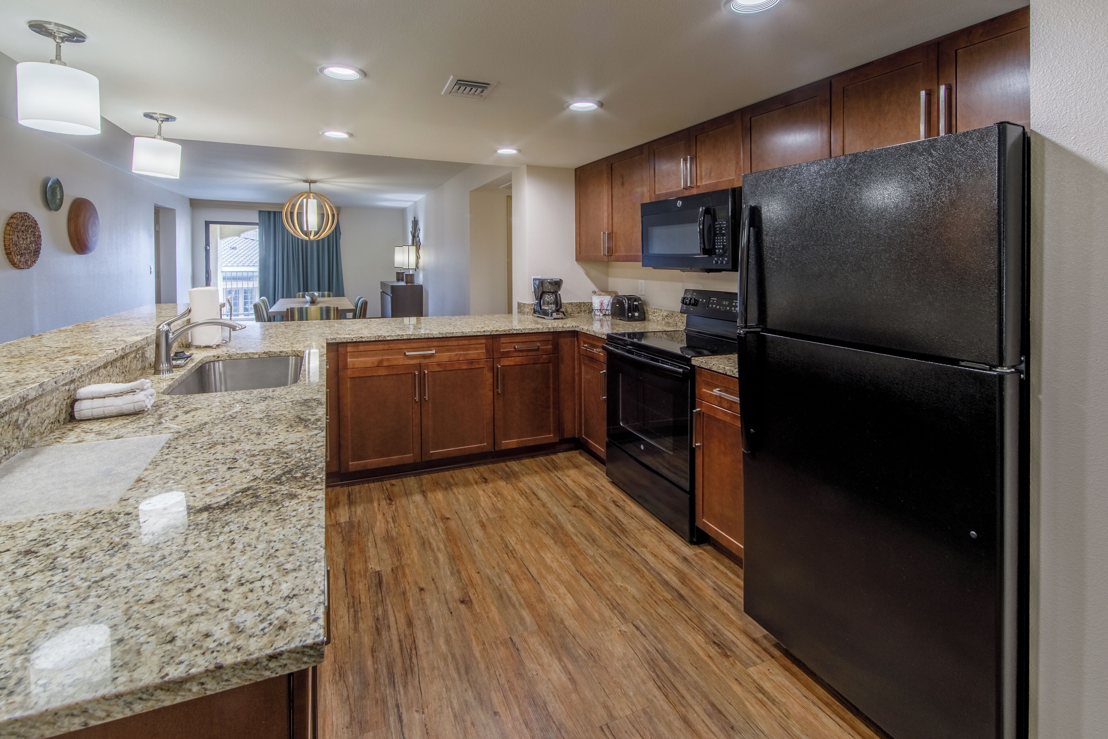 A modern kitchen with granite countertops, wooden cabinets, a black refrigerator, and a built-in oven.