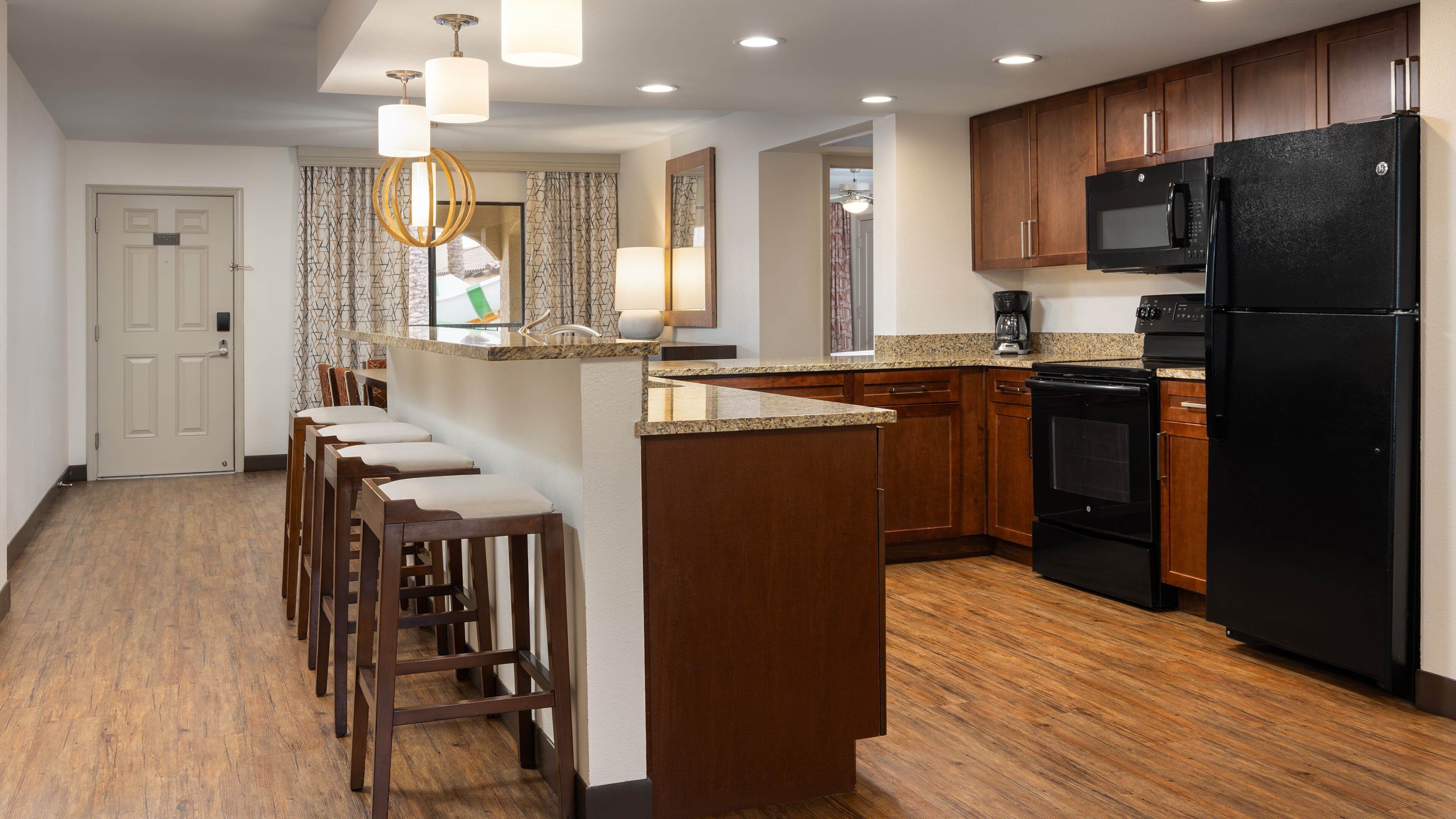 A modern kitchen with wooden cabinets, a black refrigerator, and a granite countertop.