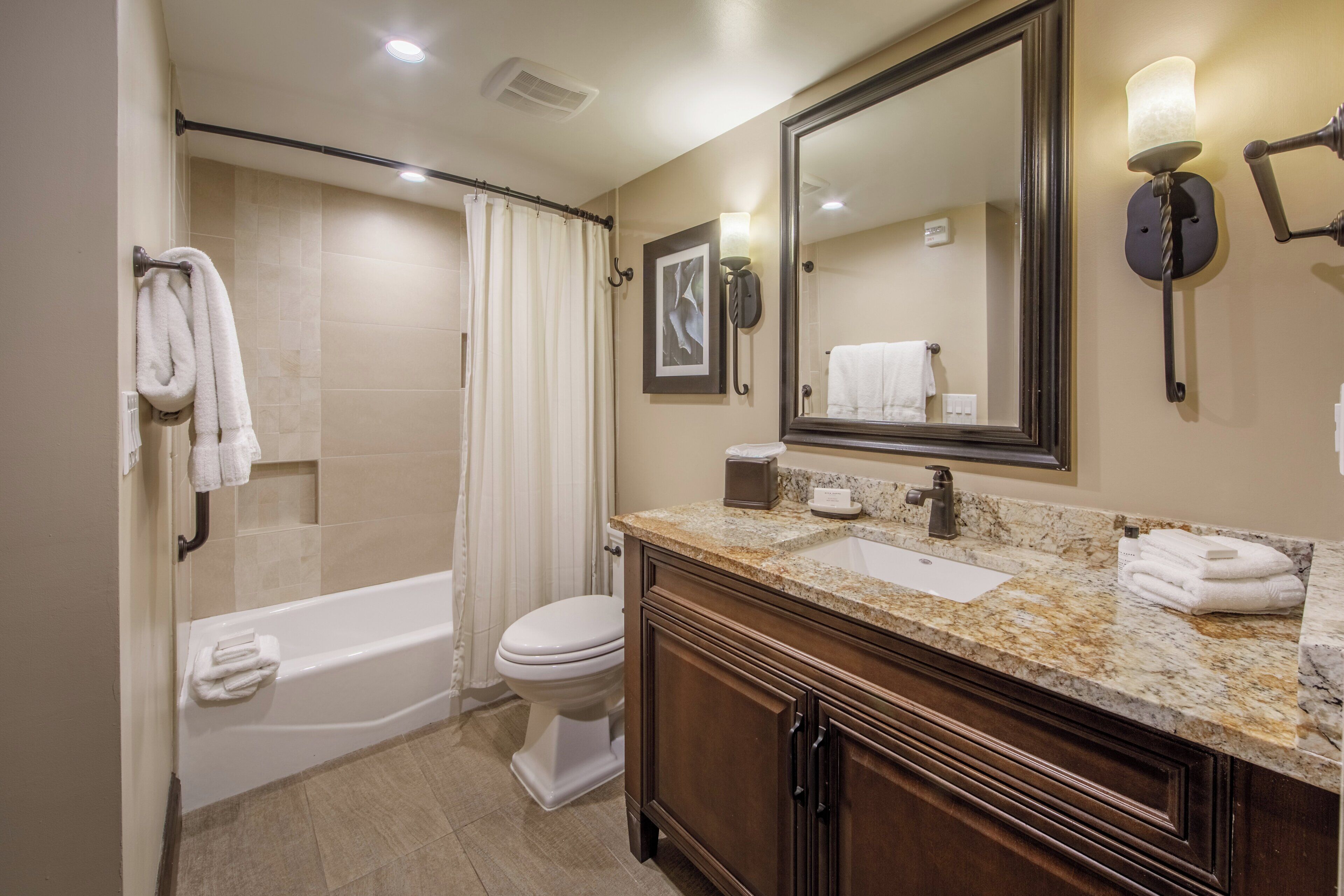 A bathroom with a bathtub, toilet, vanity with a mirror, and a shower curtain.