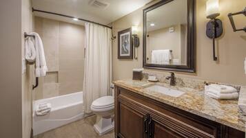 A bathroom with a bathtub, toilet, vanity with a mirror, and a shower curtain.