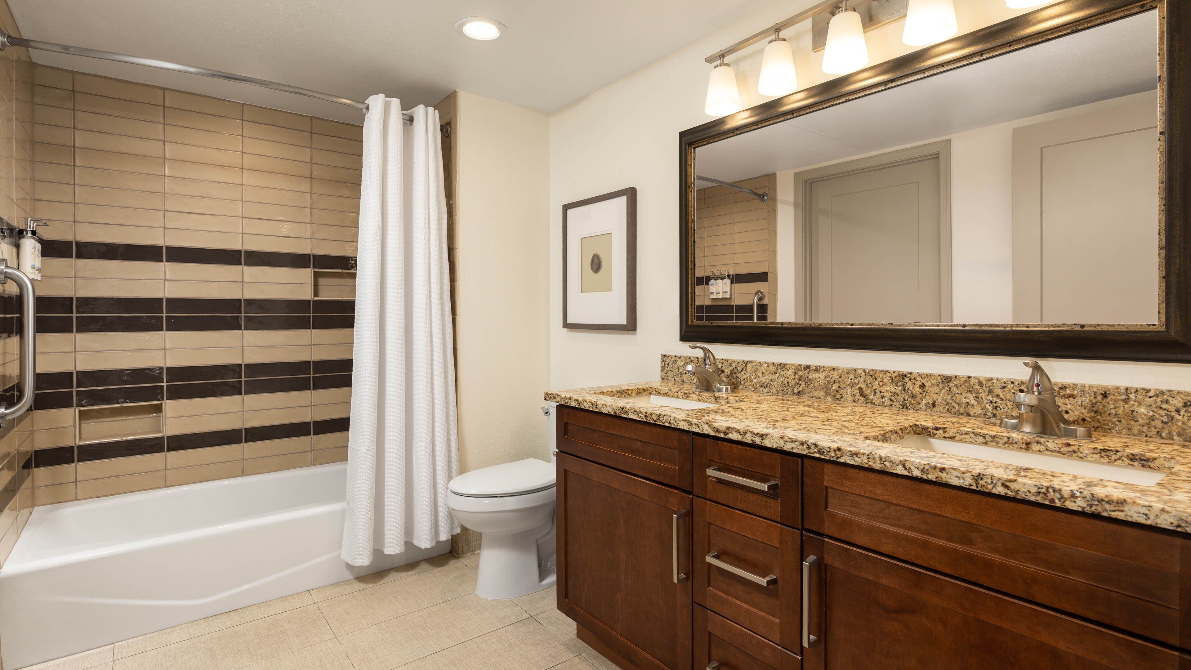 A bathroom with a bathtub, toilet, vanity with a sink, and a large mirror.