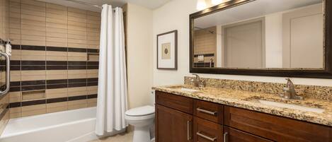 A bathroom with a bathtub, toilet, vanity with a sink, and a large mirror.