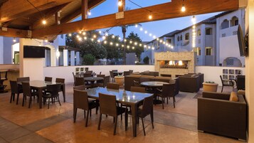 An outdoor patio with tables and chairs, a brick fireplace, and string lights.