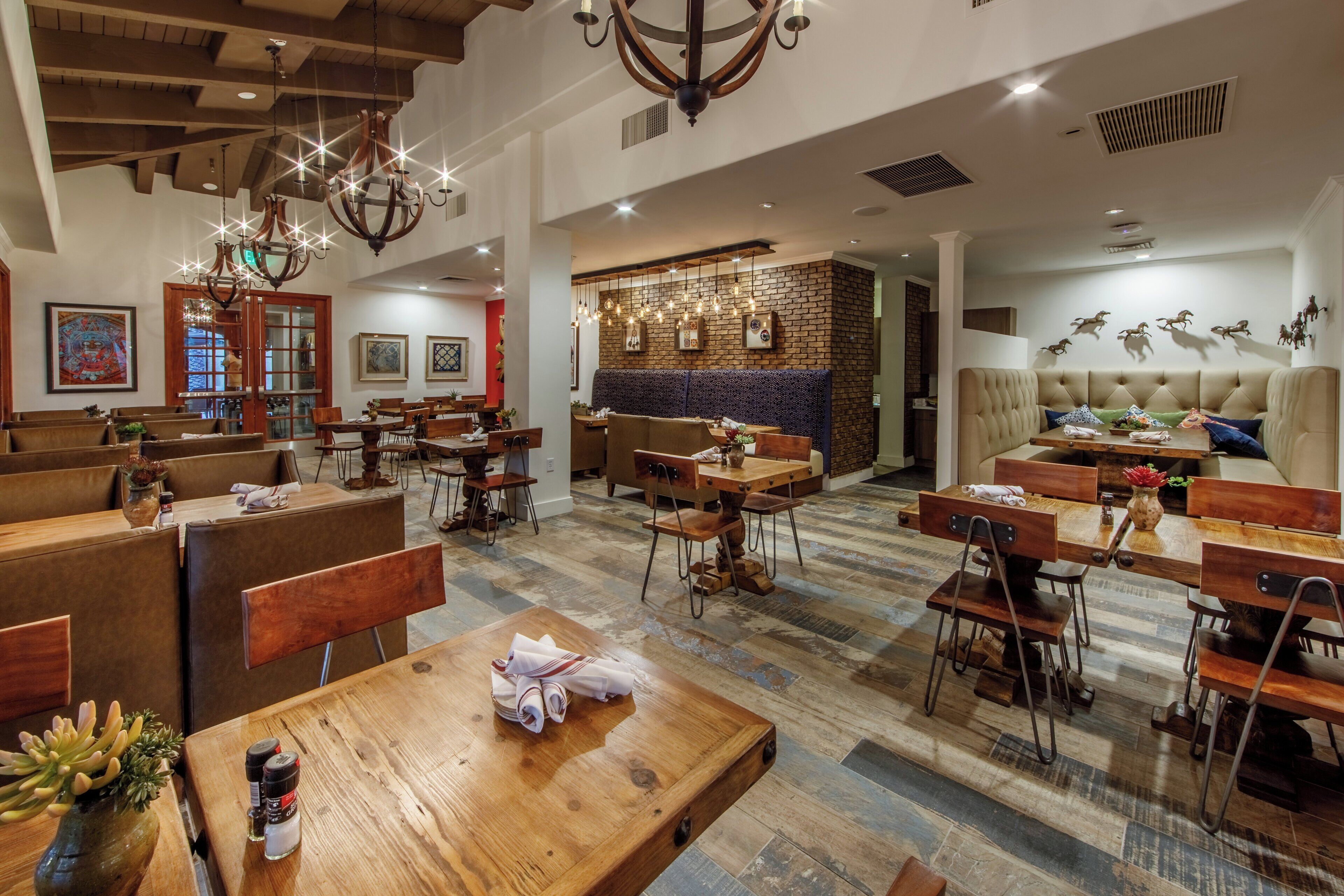 A restaurant interior with wooden tables, benches, and a brick wall.