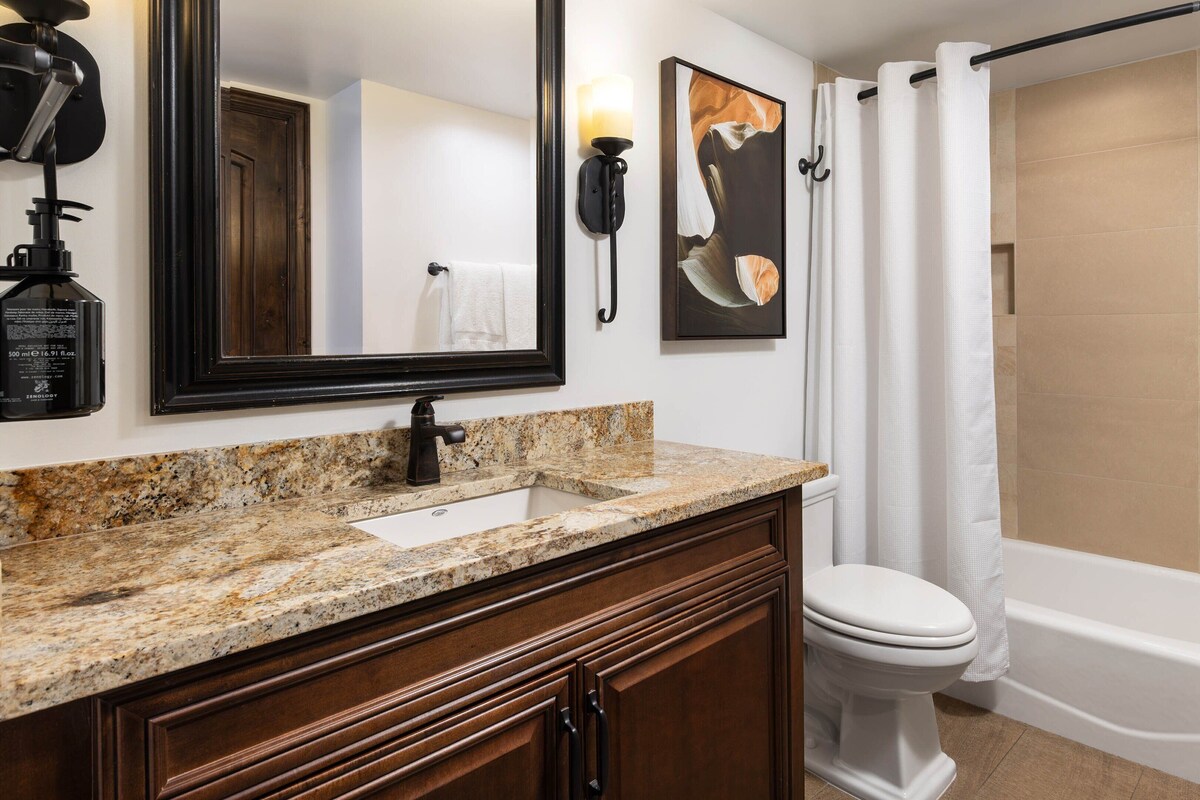 Une salle de bain avec un lavabo à vasque en granit, un meuble-lavabo en bois foncé, des toilettes blanches, une baignoire et un rideau de douche.