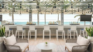 A bar area with a view of the ocean, featuring wicker chairs, a round table, and a bar stocked with bottles. - San Juan Marriott Resort and Stellaris Casino (San Juan)