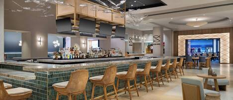 Eine moderne Bar mit einer langen Theke, mehreren Barhocker und einer Auswahl an Flaschen.