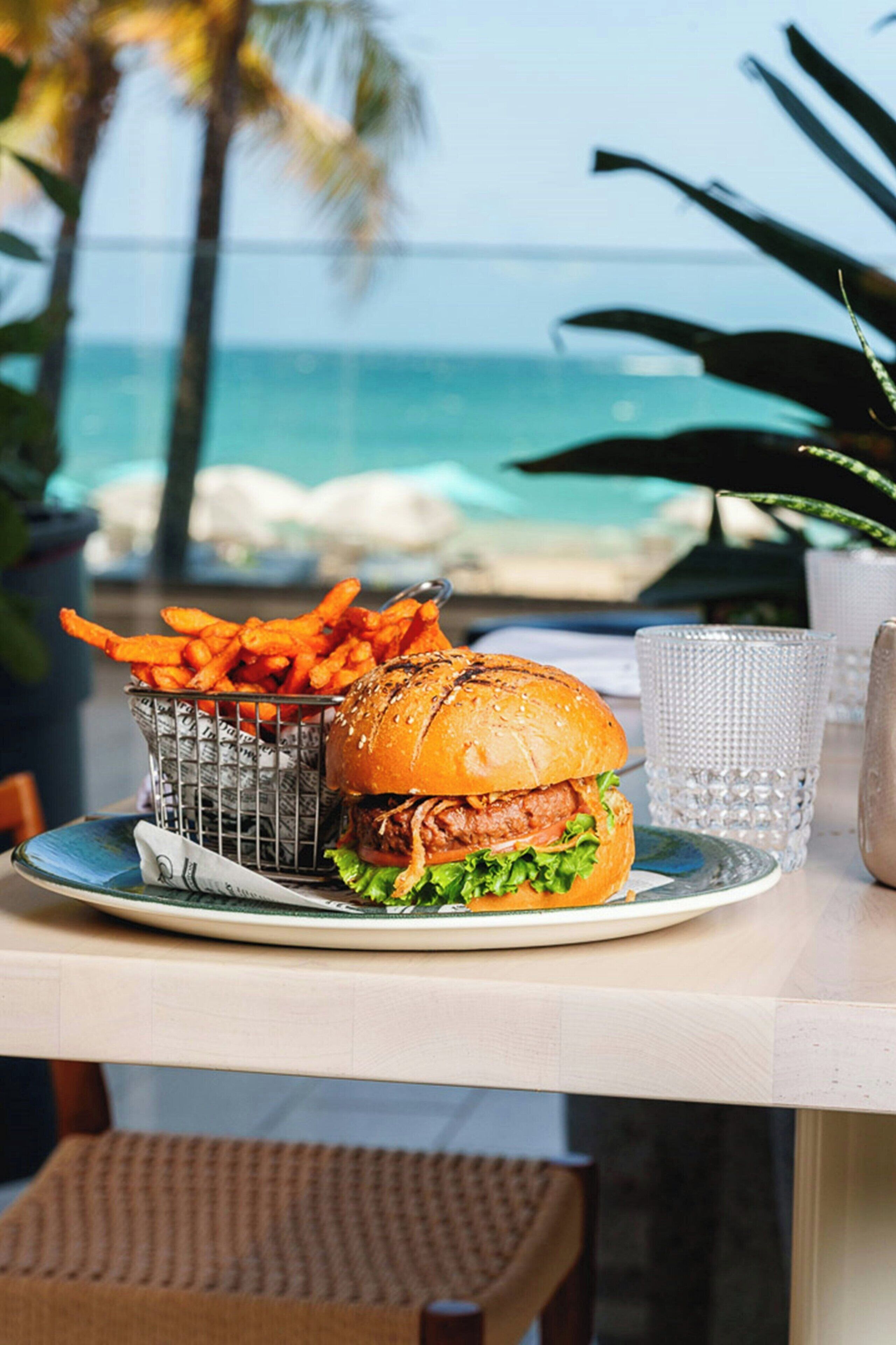 A meal of a burger and fries on a table with a view of the ocean.