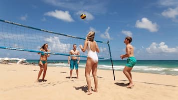 A beach volleyball game with players in swimwear on a sandy beach with a clear sky.