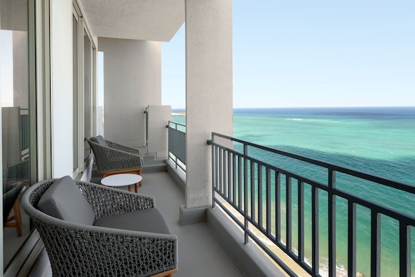 A balcony with wicker furniture, a small table, and a view of the ocean.