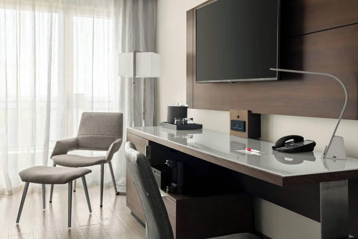 Ein Hotelzimmer mit Schreibtisch, zwei Stühlen, einem Flachbildfernseher, einer Lampe, einer Kaffeemaschine und einem Telefon.