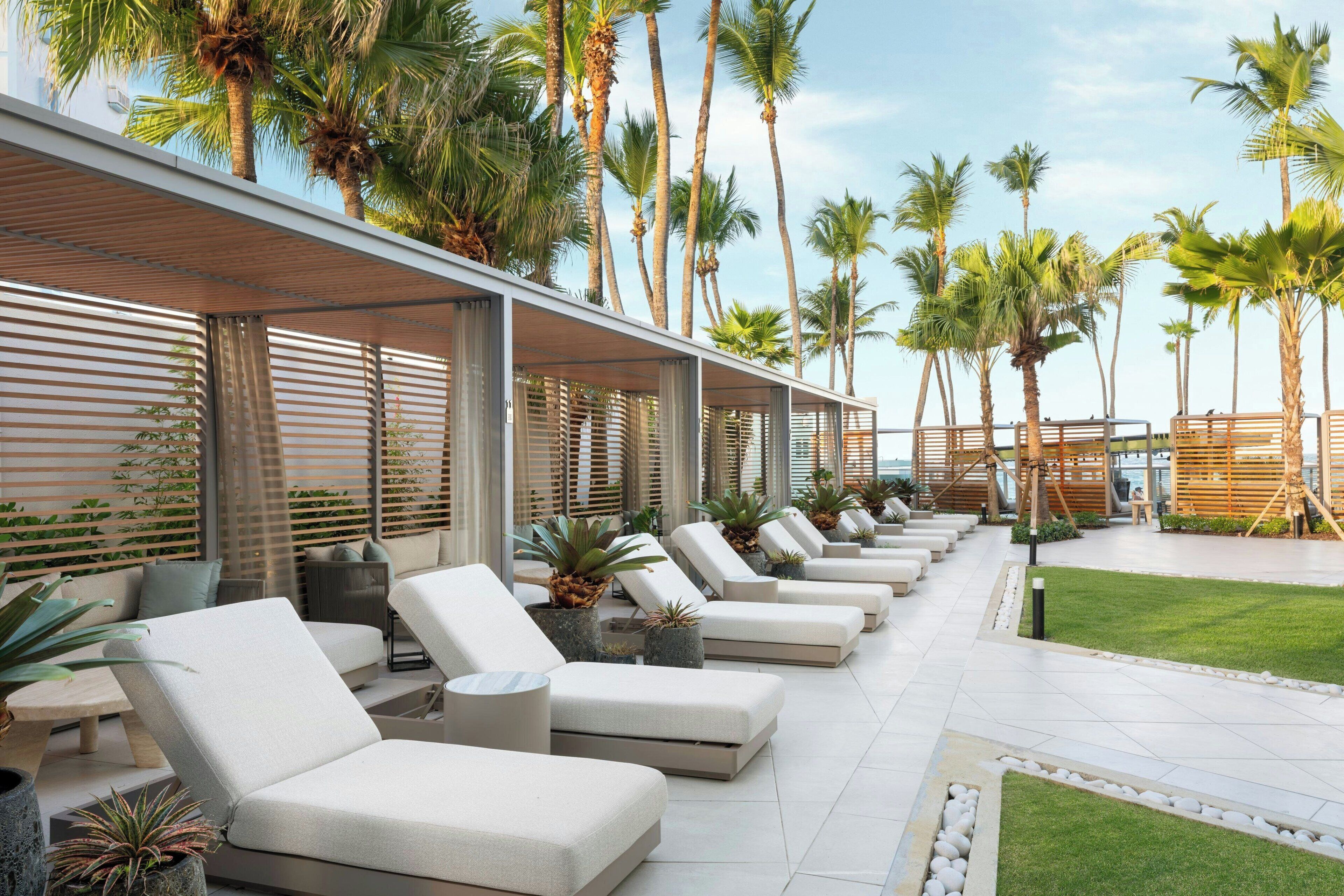 A row of white lounge chairs with a view of palm trees and a grassy area.