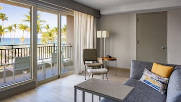 Una habitación de hotel moderna con balcón, un sofá, una silla, una mesita y una lámpara.