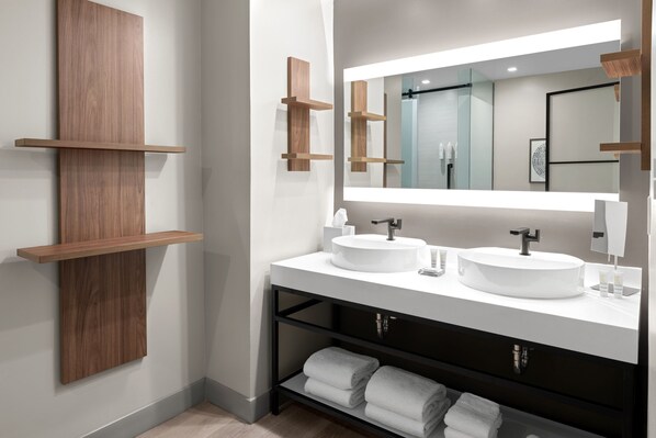 Ein modernes Badezimmer mit zwei Waschbecken, einem großen Spiegel, Holzregalen und ordentlich gefalteten Handtüchern.