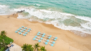 An aerial view of a beach with rows of sun loungers and umbrellas, palm trees, and waves approaching the shore. - San Juan Marriott Resort and Stellaris Casino (San Juan)