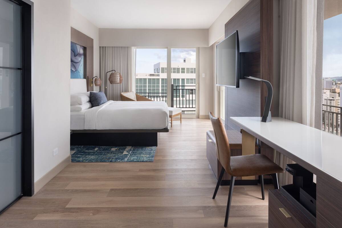 Ein modernes Hotelzimmer mit einem großen Bett, einem Schreibtisch und Blick auf die Stadt.