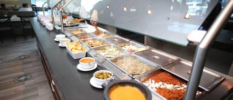 A buffet line with various food options and a staff member serving.