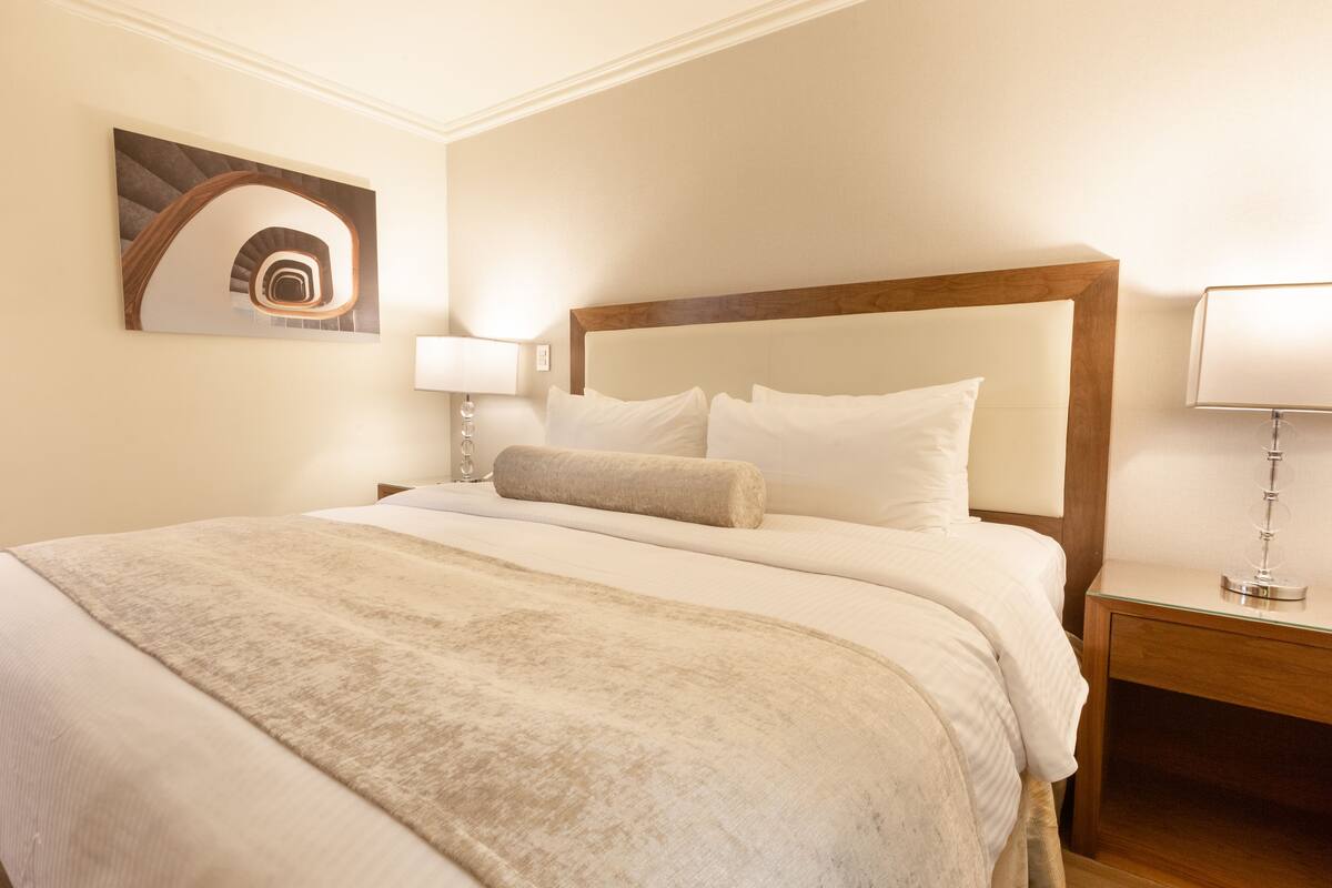 A neatly made bed with a wooden headboard, a bedside lamp, and a wall-mounted artwork of a spiral staircase.