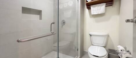 Un baño con cabina de ducha de vidrio, inodoro y estante con toallas dobladas.