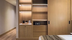 Una habitación de hotel con un armario de madera, una mesita de noche con lámpara y una cama con manta a rayas.