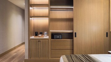 A hotel room with a wooden wardrobe, a bedside table with a lamp, and a bed with a striped blanket.
