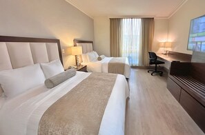 Habitación de hotel con dos camas, un escritorio, una silla, un televisor y una ventana con cortinas.