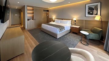 Una habitación de hotel moderna con cama, mesitas de noche, escritorio, silla, una mesa redonda y televisor montado en la pared.